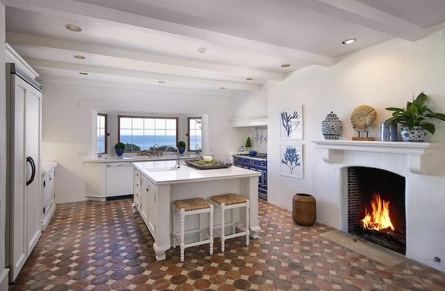 kitchen featuring a kitchen bar, white cabinetry, a center island with sink, white dishwasher, and beam ceiling