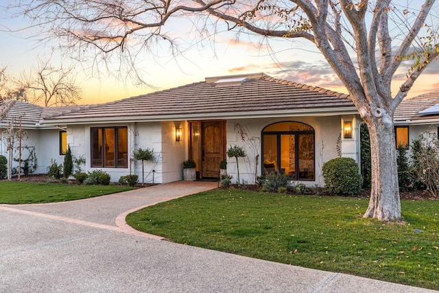 view of front of home featuring a tile roof, a lawn, and stucco siding