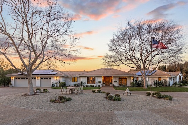 view of front of home featuring a garage, driveway, a tile roof, and solar panels