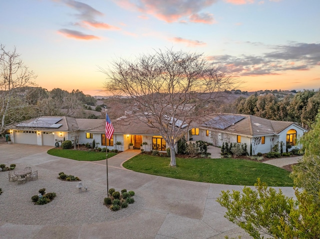 ranch-style house featuring concrete driveway, a tile roof, an attached garage, roof mounted solar panels, and a front lawn