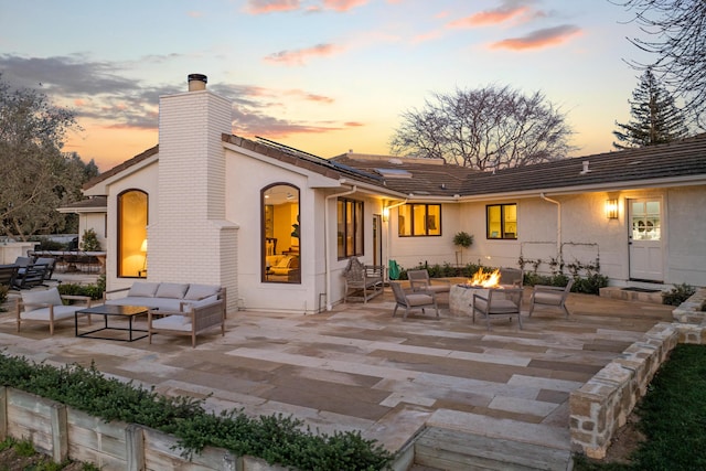 back of property at dusk with an outdoor living space with a fire pit, a chimney, stucco siding, and a patio