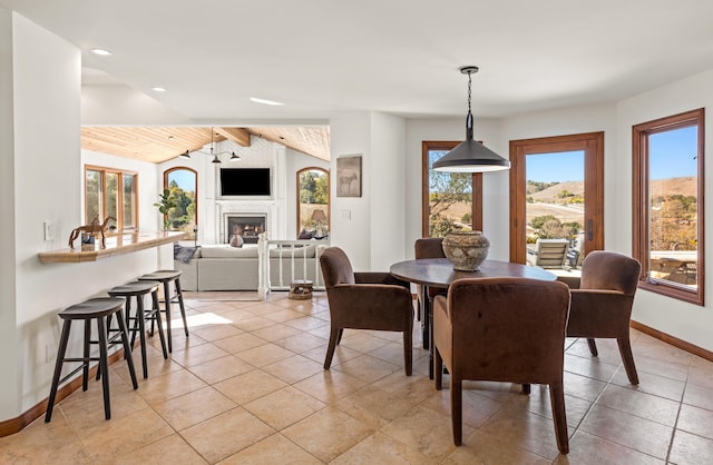 dining room featuring vaulted ceiling with beams, light tile patterned floors, a lit fireplace, and baseboards