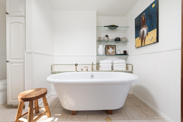 full bath with wainscoting, a soaking tub, tile patterned flooring, and toilet