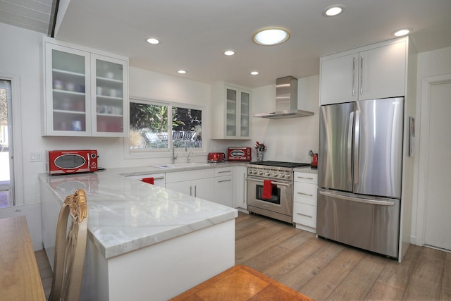 kitchen featuring white cabinetry, sink, stainless steel appliances, wall chimney range hood, and light hardwood / wood-style flooring