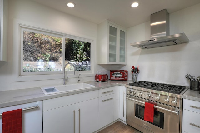 kitchen featuring sink, high end stainless steel range oven, light stone counters, white cabinets, and wall chimney exhaust hood