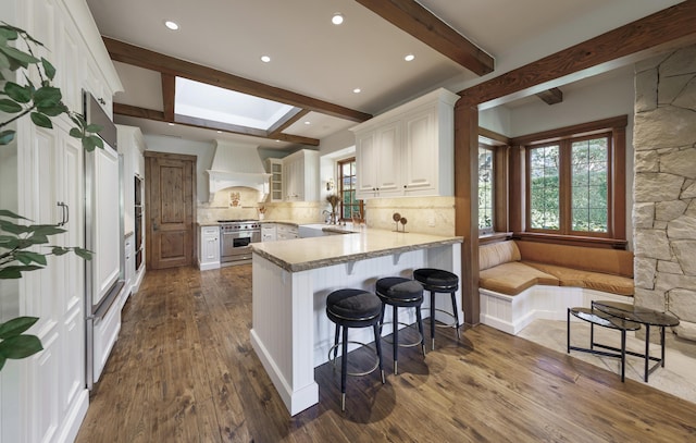 kitchen with a kitchen bar, white cabinetry, kitchen peninsula, custom range hood, and backsplash