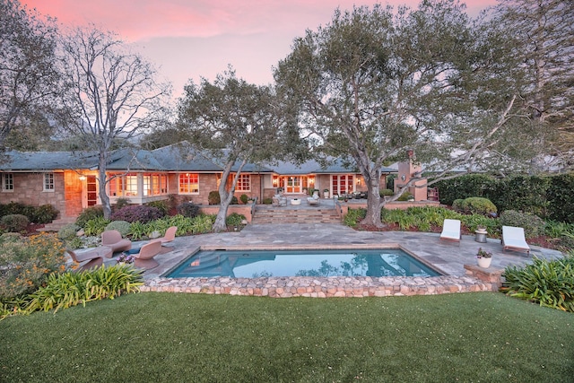 pool at dusk with a yard and a patio area