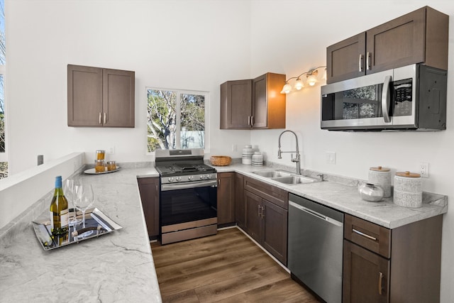 kitchen with appliances with stainless steel finishes, sink, light stone counters, dark brown cabinetry, and dark wood-type flooring