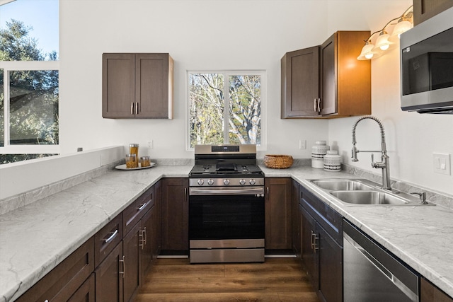 kitchen with sink, appliances with stainless steel finishes, dark hardwood / wood-style floors, dark brown cabinetry, and light stone countertops