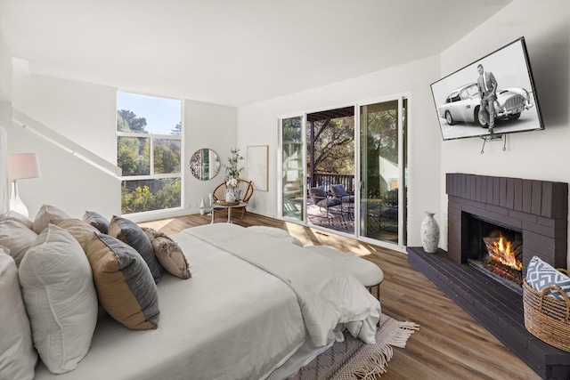 bedroom featuring wood-type flooring, a brick fireplace, and access to outside