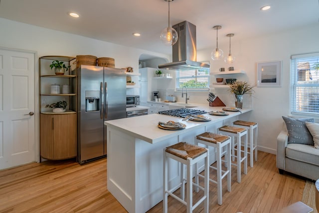 kitchen with a kitchen bar, island range hood, decorative light fixtures, kitchen peninsula, and stainless steel appliances