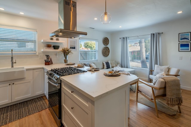 kitchen with stainless steel gas range, sink, white cabinetry, decorative light fixtures, and island exhaust hood