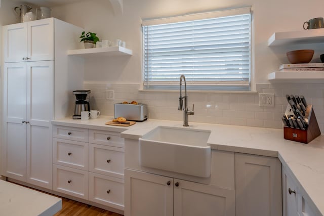 kitchen featuring tasteful backsplash, white cabinetry, light stone countertops, and sink