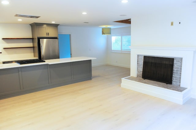 kitchen featuring gray cabinetry, a fireplace, stainless steel refrigerator, and light wood-type flooring