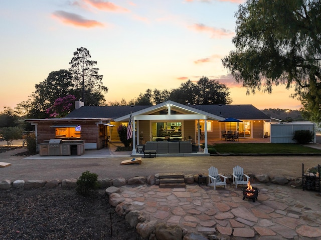 back house at dusk with exterior kitchen, a patio, and an outdoor living space with a fire pit