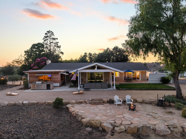 back house at dusk featuring an outdoor kitchen, a patio, and an outdoor living space with a fire pit