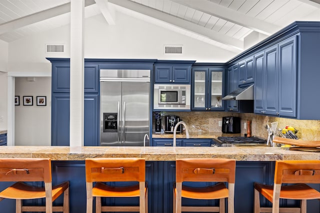 kitchen featuring a breakfast bar, vaulted ceiling with beams, backsplash, built in appliances, and blue cabinetry