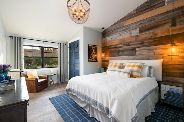 bedroom featuring lofted ceiling, wooden walls, an inviting chandelier, and light hardwood / wood-style flooring