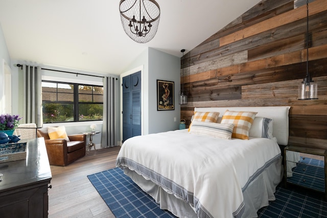 bedroom with vaulted ceiling, wood walls, a closet, a notable chandelier, and light hardwood / wood-style flooring