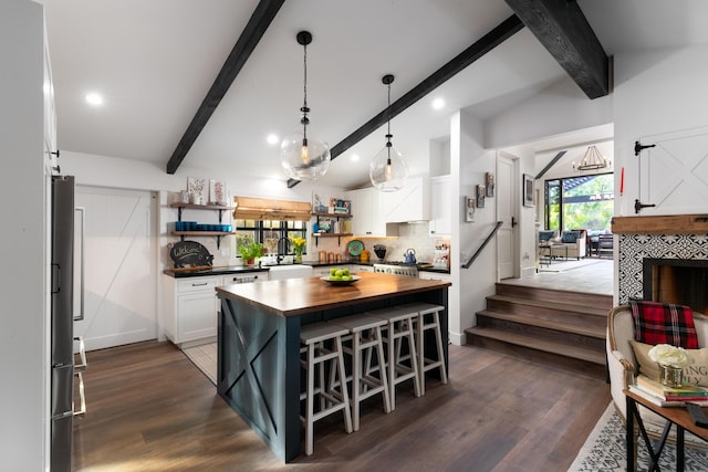 kitchen featuring a kitchen bar, butcher block counters, vaulted ceiling with beams, white cabinetry, and a center island