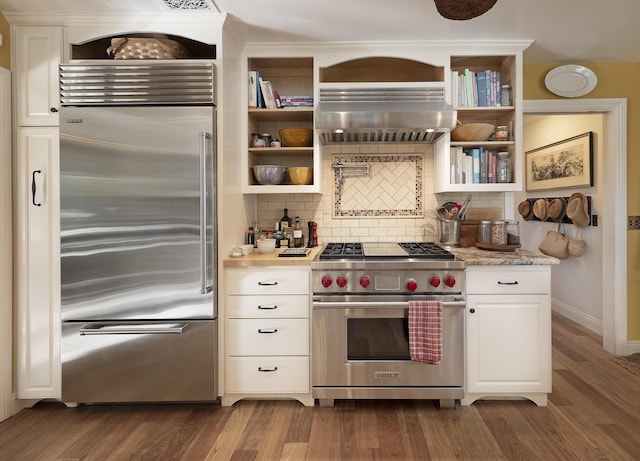 kitchen with extractor fan, backsplash, dark hardwood / wood-style flooring, white cabinets, and premium appliances