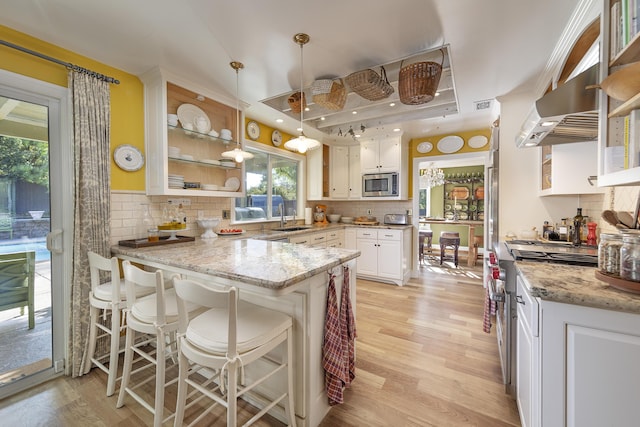 kitchen with sink, kitchen peninsula, pendant lighting, stainless steel appliances, and white cabinets