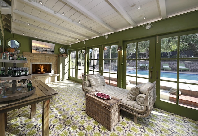 sunroom with french doors, track lighting, beam ceiling, and a stone fireplace