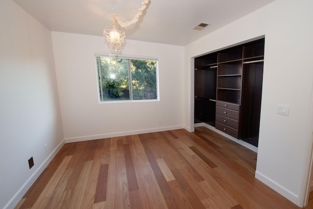 unfurnished bedroom featuring an inviting chandelier, wood-type flooring, and a closet