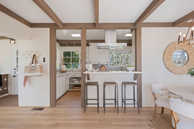 kitchen featuring backsplash, white cabinetry, island range hood, kitchen peninsula, and a breakfast bar area