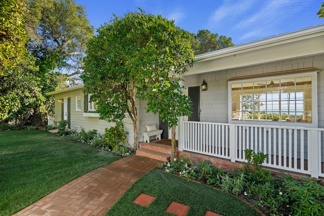 view of exterior entry with a lawn and a porch