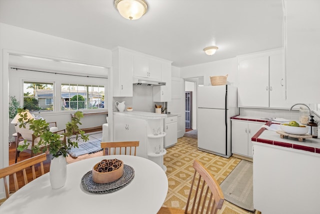 kitchen with sink, white cabinets, decorative backsplash, tile countertops, and white fridge