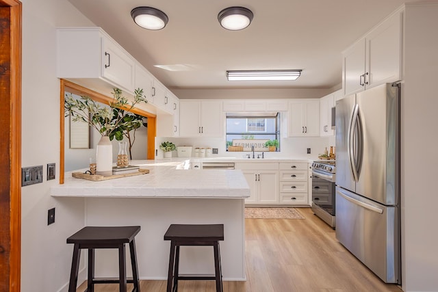 kitchen featuring a breakfast bar area, white cabinetry, light wood-type flooring, appliances with stainless steel finishes, and kitchen peninsula