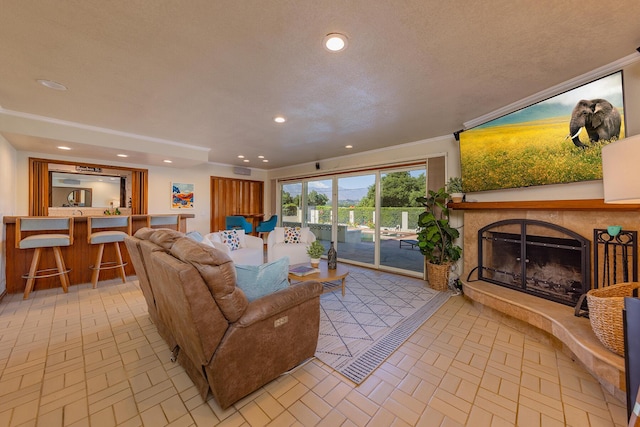 living room featuring a tiled fireplace, crown molding, and bar area