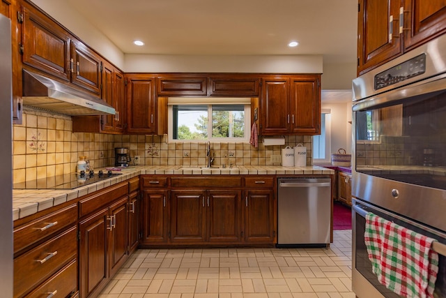 kitchen with tasteful backsplash, appliances with stainless steel finishes, tile countertops, and sink