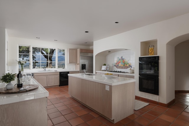 kitchen featuring light brown cabinetry, sink, a kitchen island with sink, decorative backsplash, and black appliances