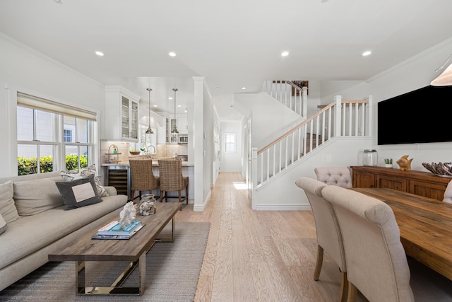 living room featuring sink, crown molding, beverage cooler, and light wood-type flooring