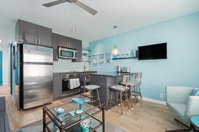 kitchen featuring appliances with stainless steel finishes, decorative light fixtures, a breakfast bar area, decorative backsplash, and kitchen peninsula