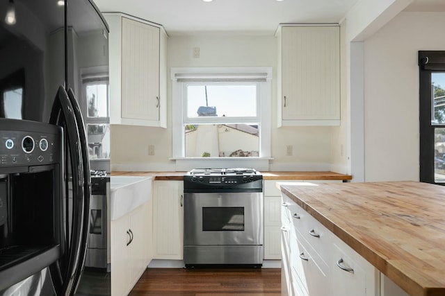 kitchen featuring butcher block counters, stainless steel stove, plenty of natural light, and black fridge