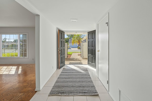 hallway featuring plenty of natural light, visible vents, baseboards, and light tile patterned flooring