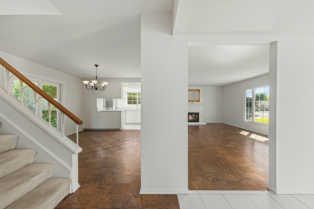 entryway featuring stairs, a fireplace, baseboards, and an inviting chandelier