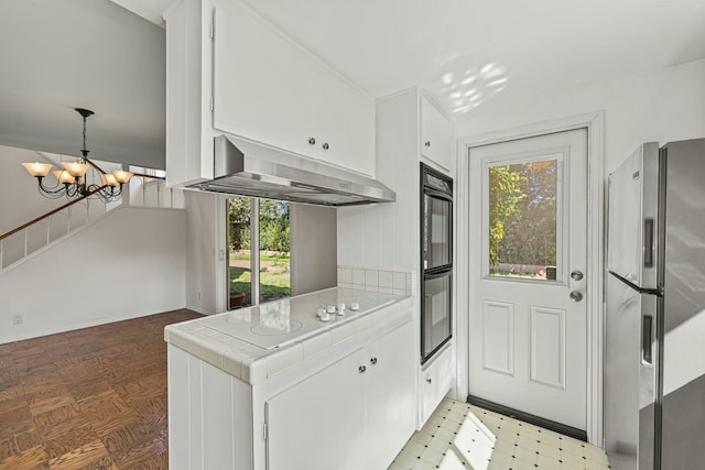 kitchen with stainless steel fridge, tile countertops, light floors, under cabinet range hood, and white cabinetry