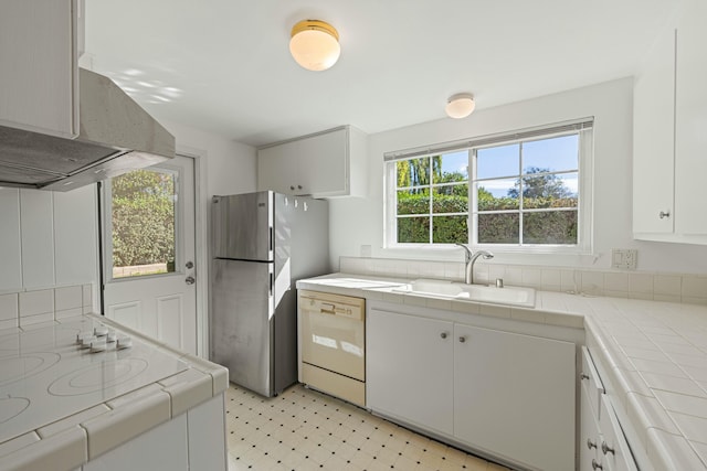 kitchen featuring light floors, tile counters, freestanding refrigerator, a sink, and dishwasher