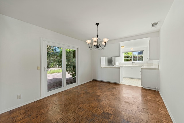 unfurnished dining area with an inviting chandelier, visible vents, baseboards, and a sink