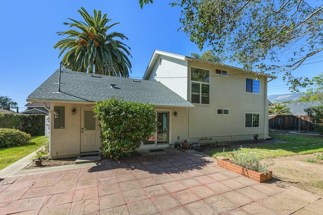 view of front facade featuring a patio, roof with shingles, fence, and stucco siding