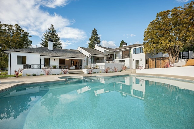 rear view of property featuring a swimming pool with hot tub and a patio area