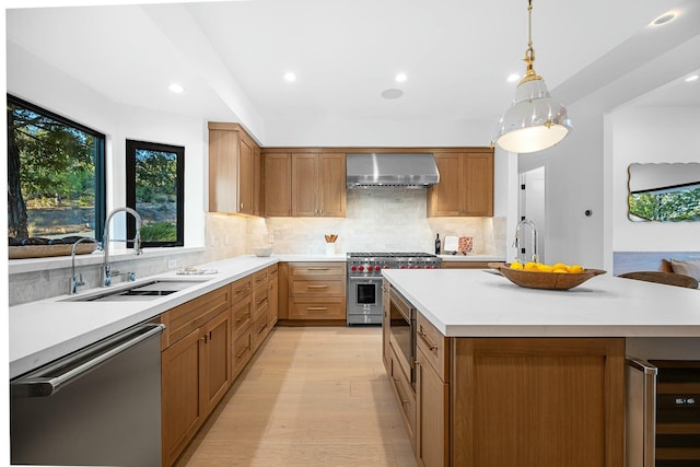 kitchen with wall chimney exhaust hood, sink, decorative light fixtures, light hardwood / wood-style flooring, and appliances with stainless steel finishes