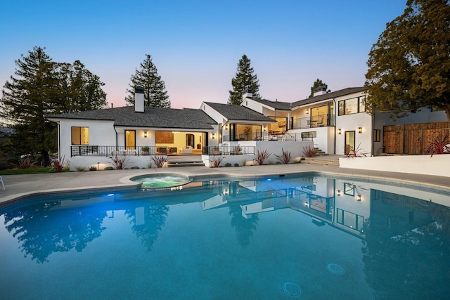 pool at dusk featuring an in ground hot tub and a patio