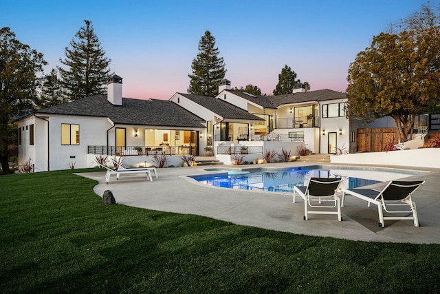 back house at dusk featuring a fenced in pool, a patio, a balcony, and a yard