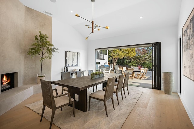 dining space featuring an inviting chandelier, a high end fireplace, high vaulted ceiling, and light wood-type flooring