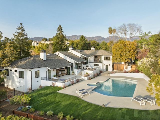 rear view of property with a swimming pool with hot tub, a lawn, an outdoor bar, a mountain view, and exterior kitchen